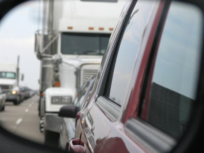 A white 18-wheeler driving behind a red vehicle